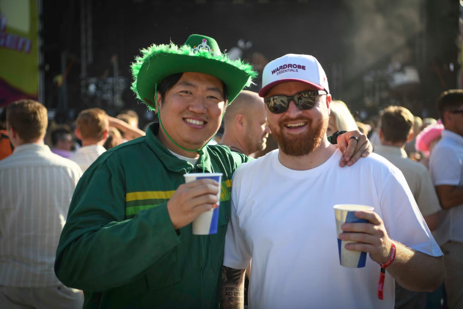 To festivalgjester med grønn hatt og drikke foran scenen