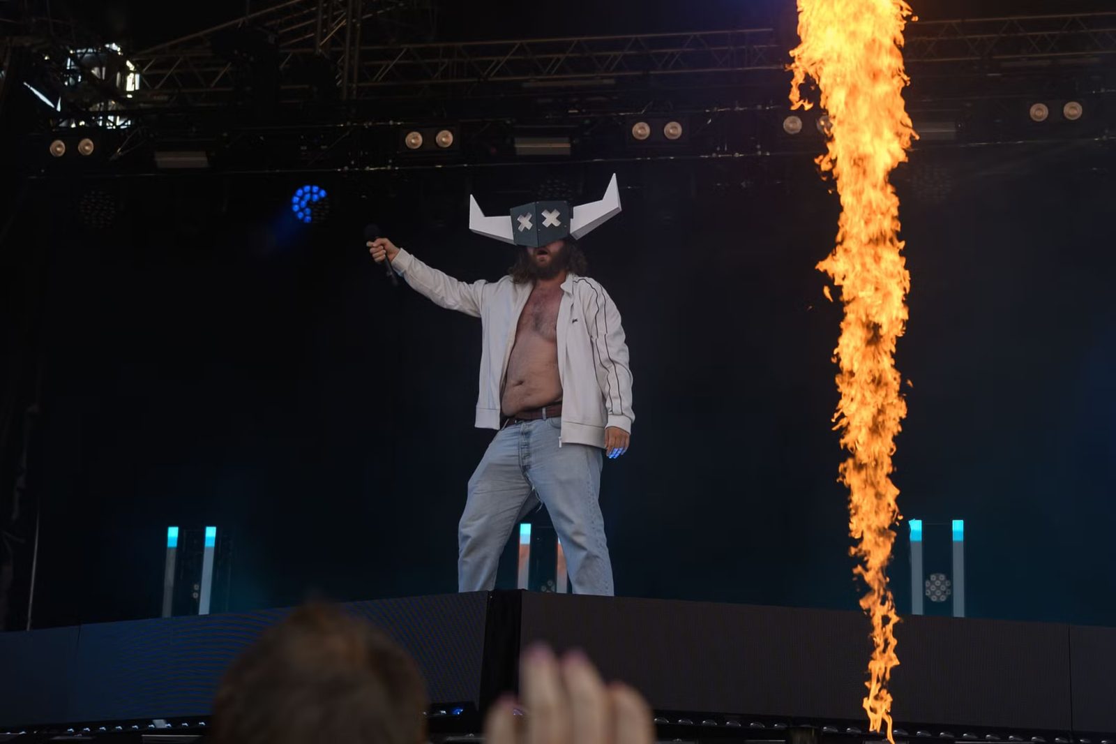 Artist med hornmaske på scenen ved siden av en flammesøyle